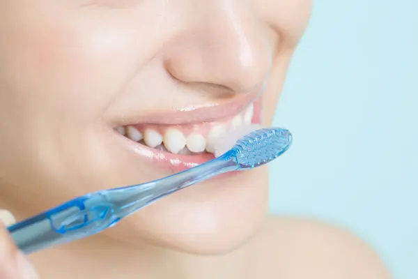 young woman brushing teeth on blue background