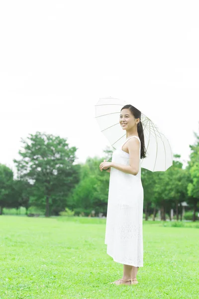 年轻的日本女人带着白色的雨伞在绿色的夏季公园里散步 身着白衣的年轻女子的白天肖像 — 图库照片