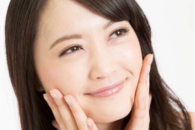 Asyalı bir kadının beyaz arka planda yüzüne dokunuşunun portresi 