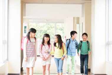 Okul koridorunda sırt çantalı bir grup Japon çocuk yürüyor. 