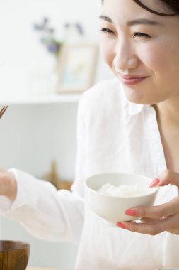 Asyalı kadın evde çubuklarla yemek yiyor.