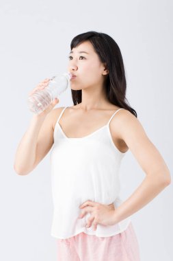 Beyaz arka planda izole edilmiş plastik şişeden su içen genç Asyalı kadın.