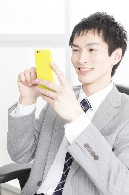 Genç Asyalı işadamı ofiste akıllı telefon kullanıyor.