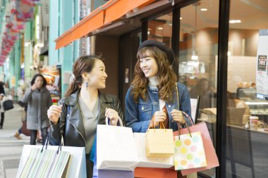 gülümseyen Asyalı genç kadınlar ellerinde alışveriş torbaları