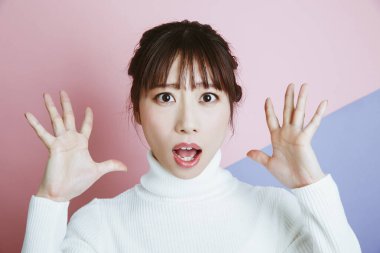 Güzel genç Asyalı kadın beyaz bir kazak giyiyor ve elleri havada. 