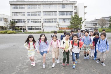 Okul bahçesinde koşan sırt çantalı bir grup Japon çocuk. 