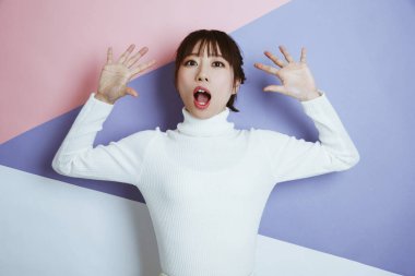 Stüdyoda elleri havada poz veren beyaz kazaklı genç bir kadının portresi. 