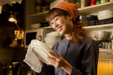 Asyalı garson kadın tabak siliyor.