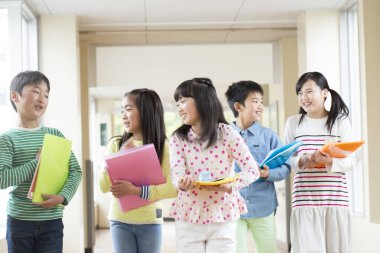 Okul koridorunda yürüyen kitaplarla bir grup Japon çocuk. 