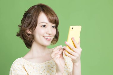 Yeşil arka planda akıllı telefon kullanan güzel bir Japon kadının portresi 