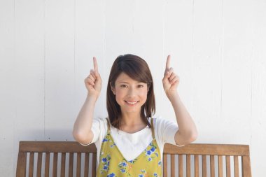 asian woman sitting on wooden bench with her hands raicing up