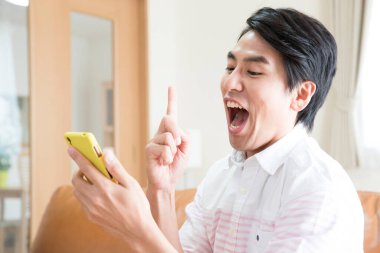 Evde akıllı telefonu olan Asyalı genç bir adam.