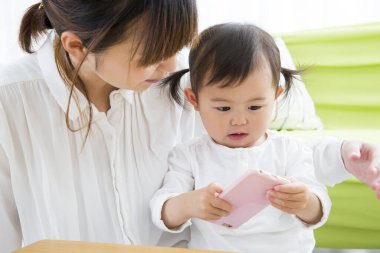 Asyalı kadın sevimli küçük kızıyla birlikte cep telefonu kullanıyor..