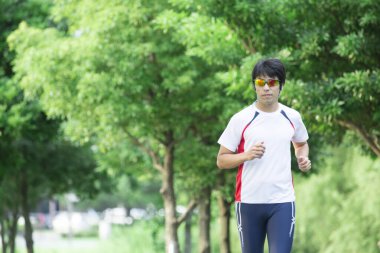 Genç yakışıklı Asyalı adam parkta koşuyor. 