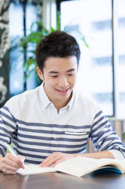 Asyalı öğrenci üniversitede masada okuyor. 