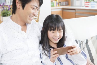 Gülümseyen baba ve kızı evde akıllı telefon kullanıyor.