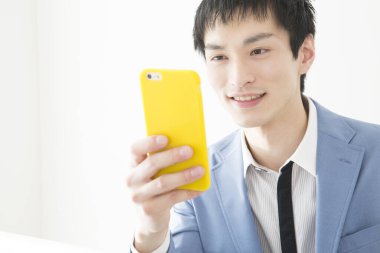 Akıllı telefon kullanan genç Japon iş adamının yakın plan portresi.