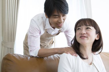 Genç adam evde Asyalı bir kadının boynuna masaj yapıyor. 