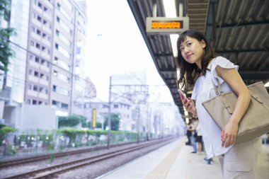 Tren istasyonunda cep telefonu olan genç Asyalı kadın.