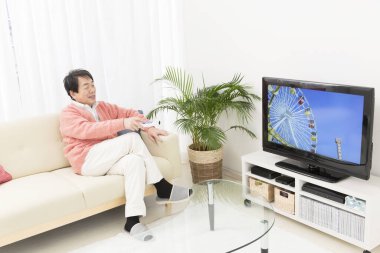 Televizyon izleyen kıdemli Asyalı adam.