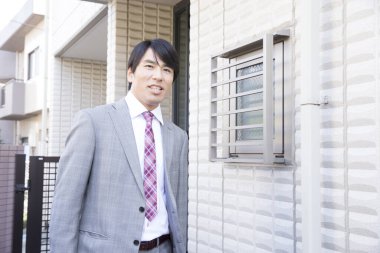 Takım elbiseli genç Japon işadamı evden ayrılıyor.