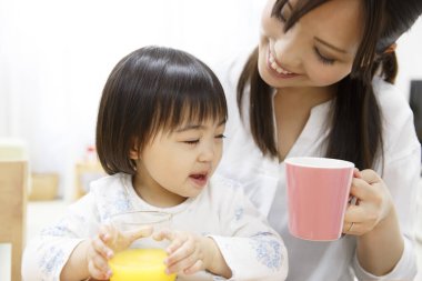 Asyalı anne ve küçük kız kahvaltı yapıyorlar. 