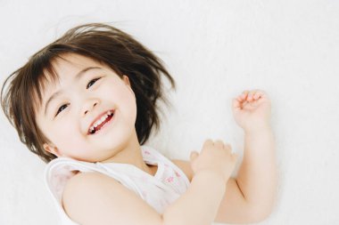 Asyalı küçük kız yatakta gülümsüyor.