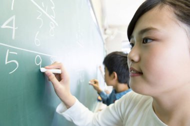 Küçük kız ve oğlan sınıfta tahtaya yazı yazıyorlar.