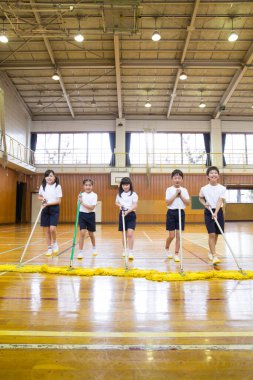 Okuldaki spor salonunu temizleyen bir grup çocuk.