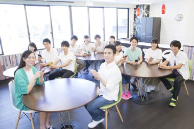 Genç Asyalı öğrenciler sınıfta akıllı telefon kullanıyorlar.