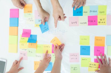 Asyalılar grubu, yapışkan notlar kullanarak beyaz tahtada beyin fırtınası yapıyor. 