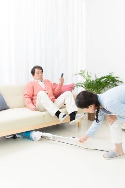 Elektrikli süpürgesi olan bir kadın ve kocası kanepede. 