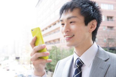 Genç Asyalı iş adamı dışarıda akıllı telefon kullanıyor.