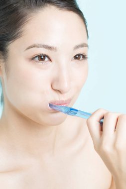 Genç kadın mavi arka plan üzerinde diş fırçalama 