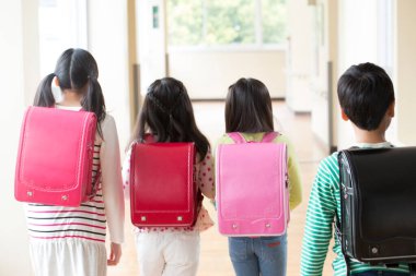 Okul koridorunda sırt çantalı bir grup Japon çocuk yürüyor. Arka plan