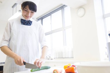 Genç Asyalı kadın aşçı üniformalı aşçı mutfakta yemek yapıyor.