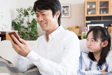 Asyalı baba ve kızı oturma odasında akıllı telefon kullanıyor.