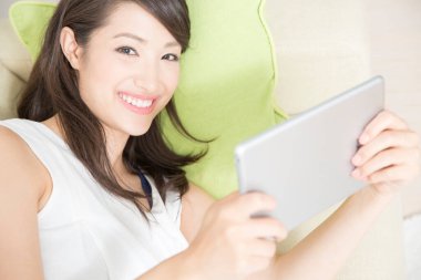 Asyalı genç bir kadın evde bir yatakta tablet bilgisayar kullanarak rahatlıyor. 