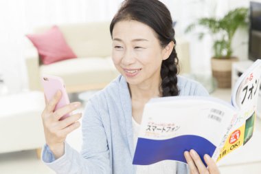 Bir mesaj okurken kitap okuyan Asyalı genç kadın. 