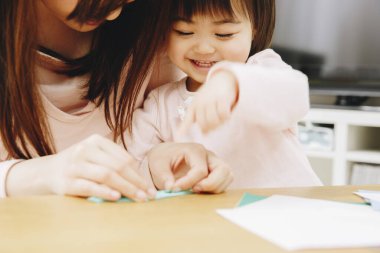 Asyalı anne ve küçük kız kağıtlarla oynuyorlar.