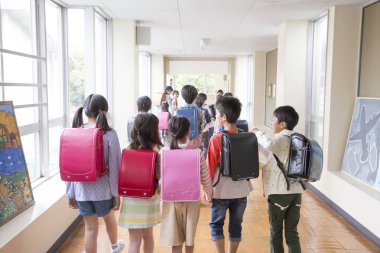 Okul koridorunda sırt çantalı bir grup Japon çocuk yürüyor. Arka plan