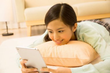 Genç Asyalı kadın oturma odasında tablet bilgisayar kullanıyor.