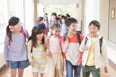 Okul koridorunda sırt çantalı bir grup Japon çocuk yürüyor. 