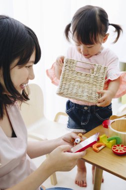 Asyalı kadın sevimli küçük kızıyla birlikte cep telefonu kullanıyor..