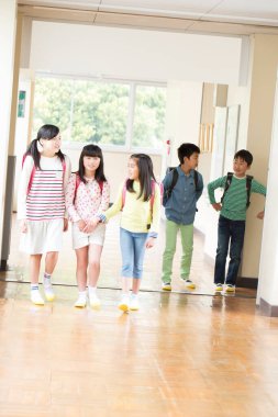 Okul koridorunda sırt çantalı bir grup Japon çocuk yürüyor. 