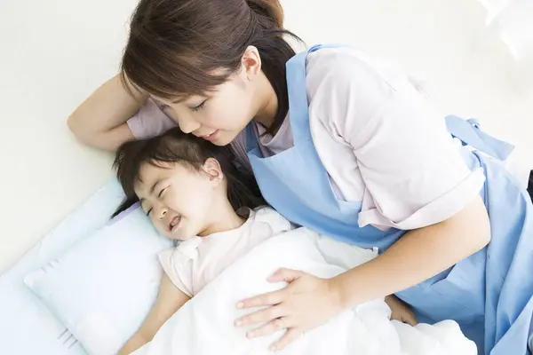 Asian young kindergarten teacher putting girl to sleep