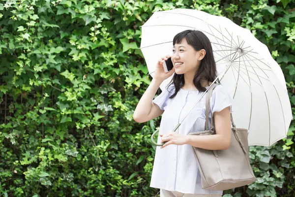 young asian woman with umbrella talking on smartphone outdoors