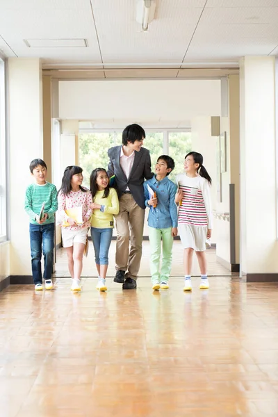Öğretmenli bir grup Japon çocuk okul koridorunda yürüyor. 