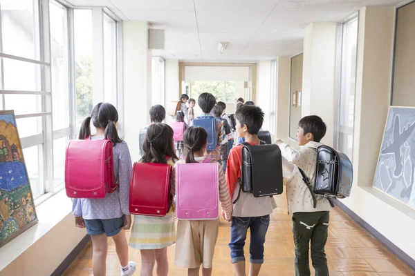 Okul koridorunda sırt çantalı bir grup Japon çocuk yürüyor. Arka plan