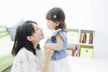 Evdeki oturma odasında annesiyle oynayan tatlı Asyalı küçük kız.